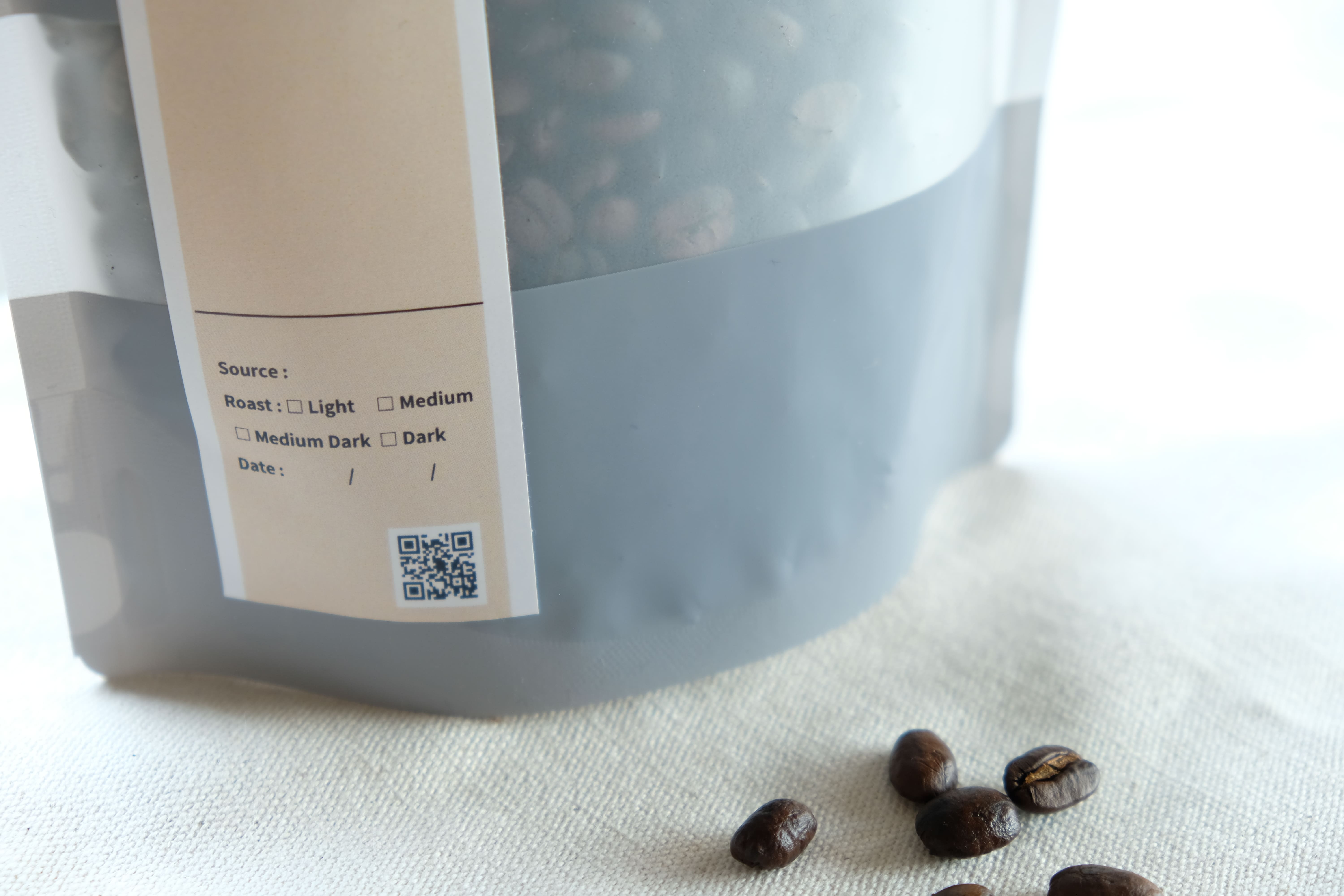 焙煎度や日付を記す商品ラベルと、布の上のコーヒー豆