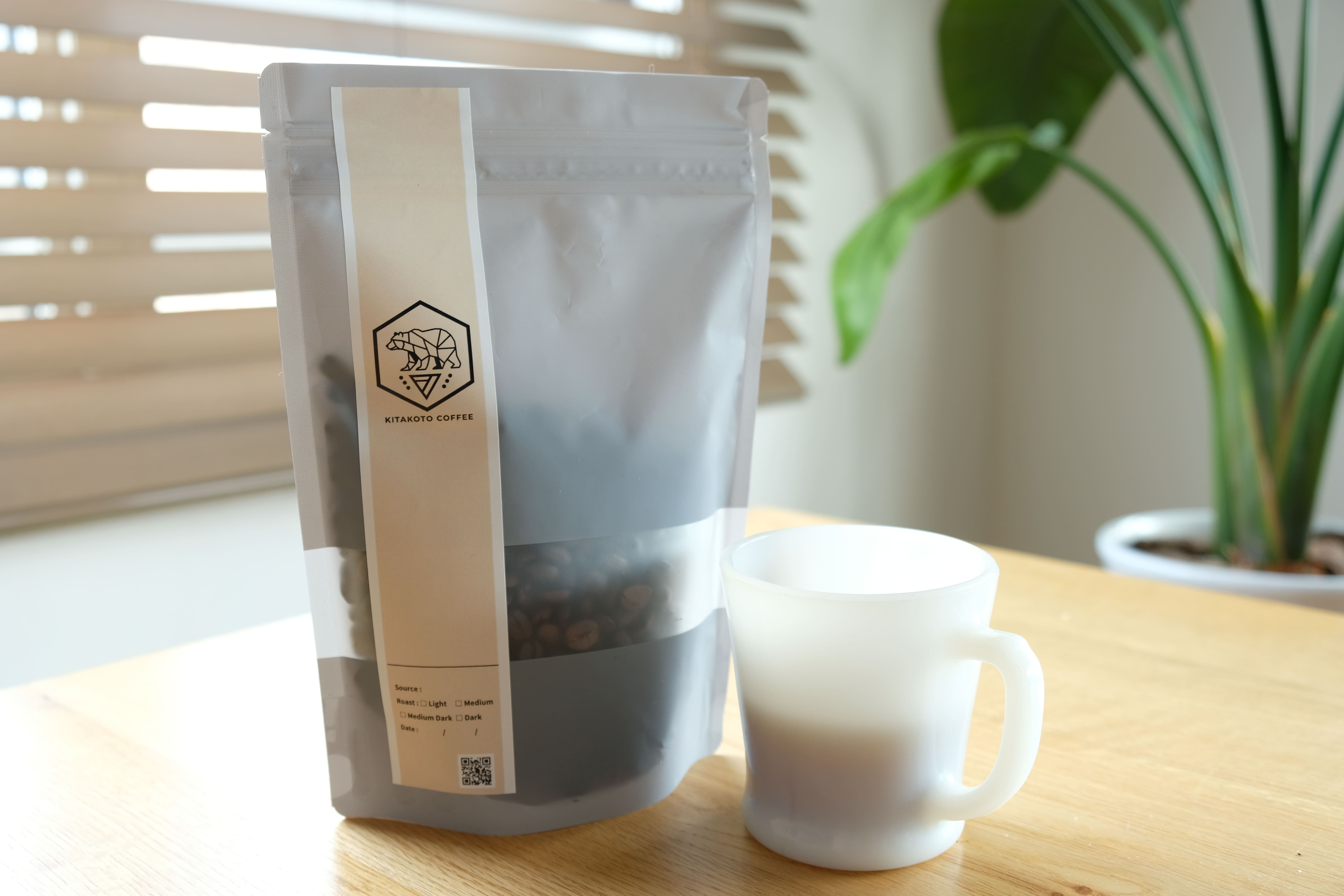 窓辺の光に包まれたKITAKOTO COFFEEの商品袋と白いカップ